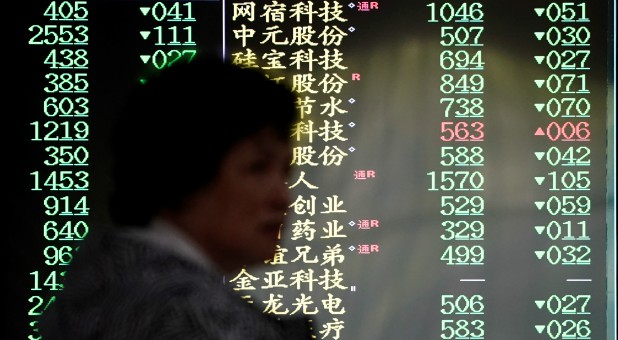 An investor walks past a screen displaying stock information at a brokerage house in Shanghai, China.