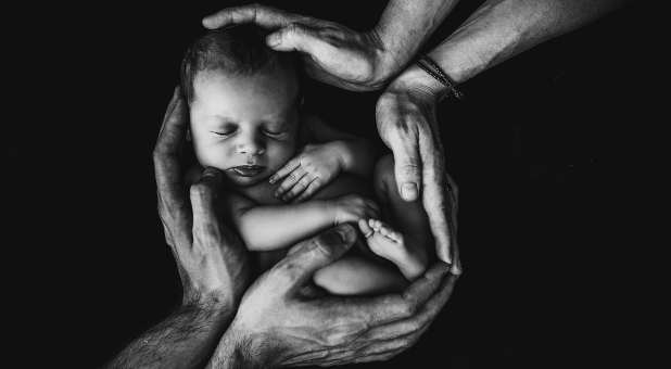 newborn baby surrounded by parents' hands