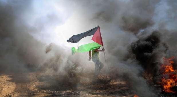 Man, surrounded by smoke and flames, carrying Palestinian flag amid attacks