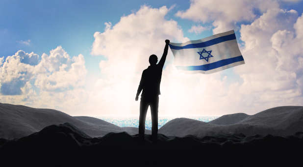 A person holding an Israeli flag on a mountain range.