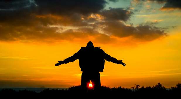 Man worshipping with arms outspread in view of sunrise.