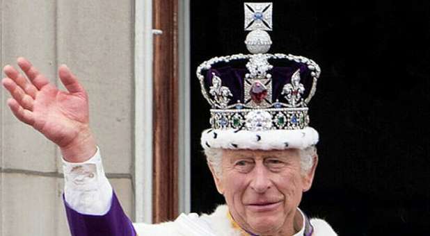 King Charles III, wearing a jewel-encrusted crown, waves from the Buckingham Palace balcony after his coronation.