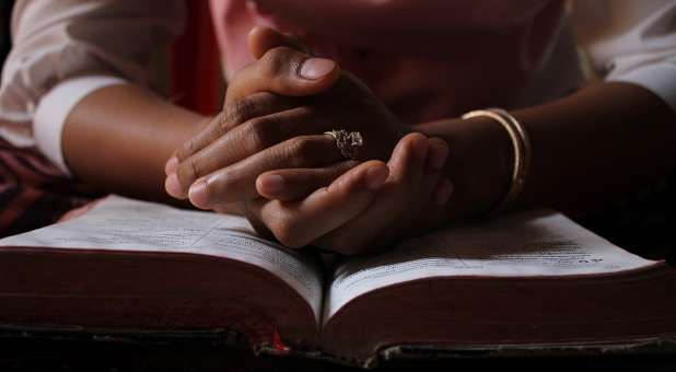 Praying hands, resting on Bible.